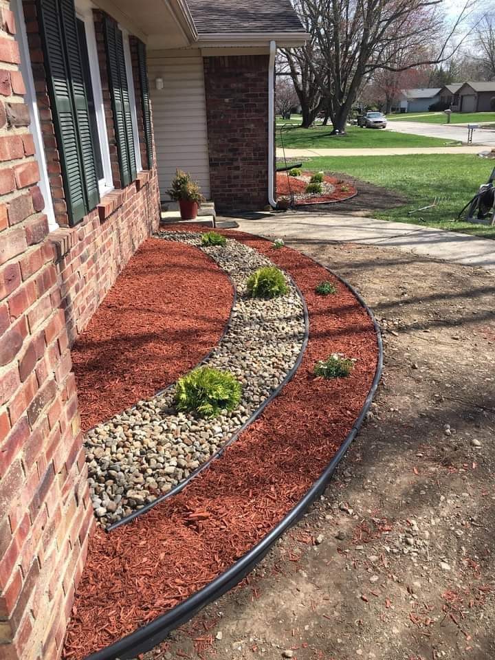 Red mulch and a curved river-stone planting bed beside a brick home